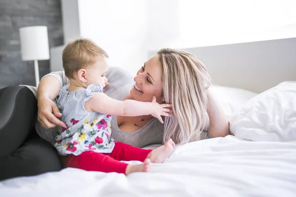 Bebê bonito sentar na mãe na cama de seda — Fotografia de Stock