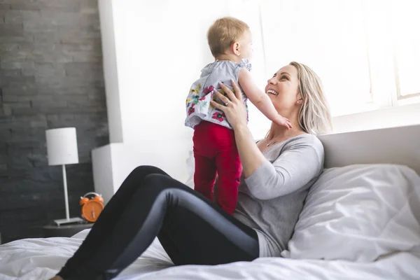 Bonito bebé sentarse en mamá en la cama de seda — Foto de Stock