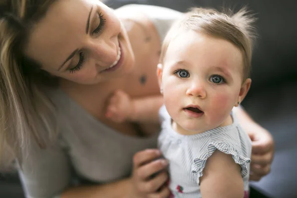 Feliz madre joven con la niña en el sofá en casa — Foto de Stock