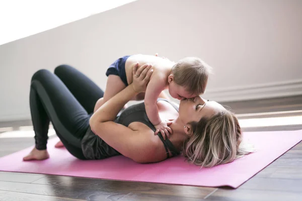 Jovem mãe faz exercícios de ioga físico junto com seu bebê — Fotografia de Stock