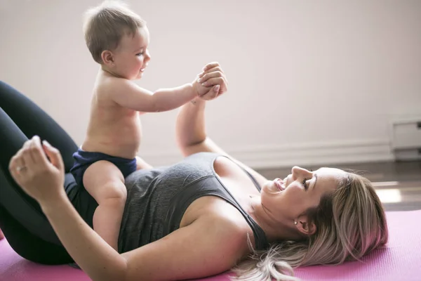 Jovem mãe faz exercícios de ioga físico junto com seu bebê — Fotografia de Stock