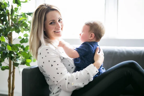 Feliz madre joven con la niña en el sofá en casa — Foto de Stock