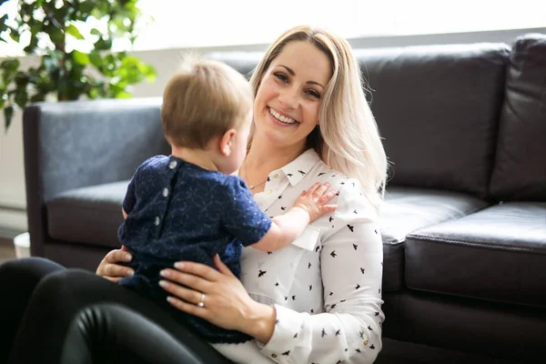 Feliz madre joven con la niña en el sofá en casa — Foto de Stock