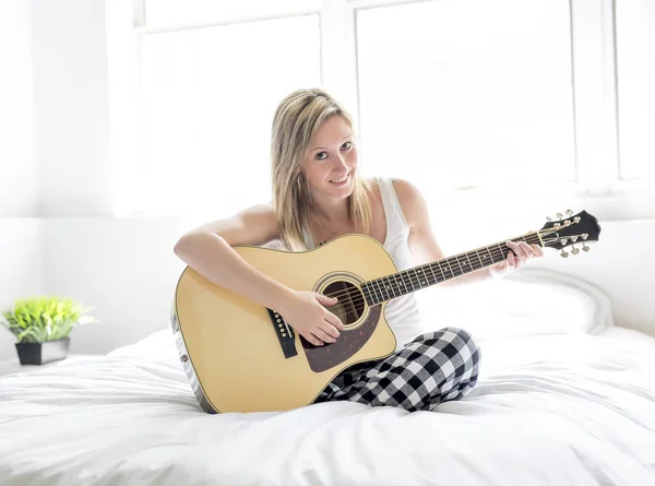 Mulher sorridente com guitarra sentada na cama — Fotografia de Stock