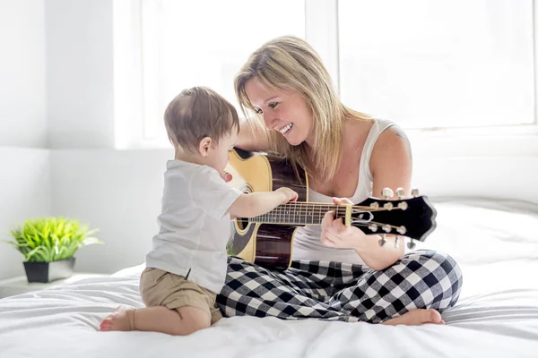 Lachende vrouw met gitaar zittend op het bed met kind — Stockfoto