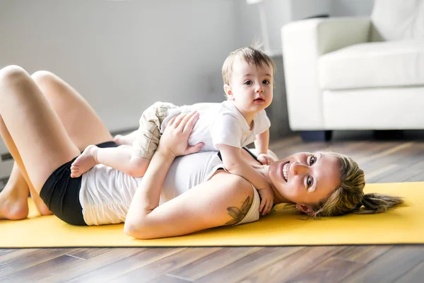 Esportes mãe está envolvida em fitness e ioga com um bebê em casa — Fotografia de Stock