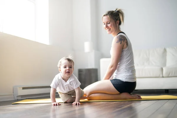 Esportes mãe está envolvida em fitness e ioga com um bebê em casa — Fotografia de Stock