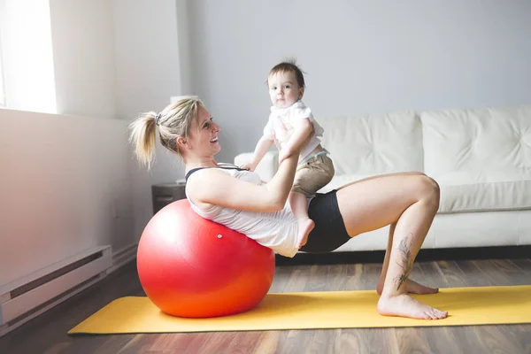 Esportes mãe está envolvida em fitness e ioga com um bebê em casa — Fotografia de Stock