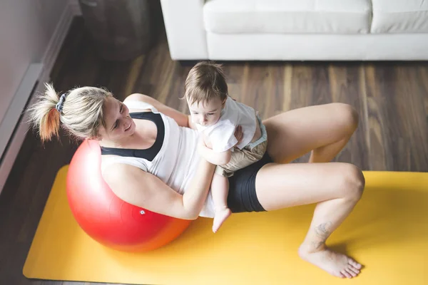 Esportes mãe está envolvida em fitness e ioga com um bebê em casa — Fotografia de Stock