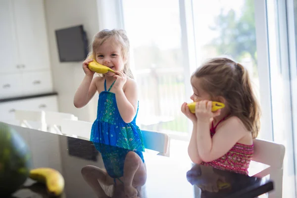 Twee meisjes met bananen op de keuken veel plezier telefoon — Stockfoto