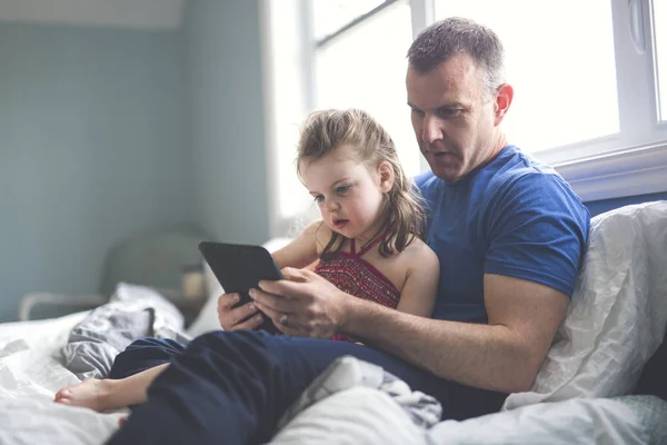 父と娘は、タブレット コンピューターが付いているベッドでリラックスします。 — ストック写真