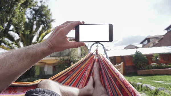 View from behind a young woman lying in a hammock and looking at smartphone — Stock Photo, Image