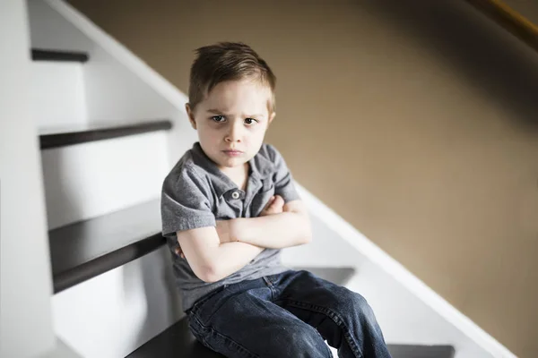 Ein trauriger kleiner Junge, der tagsüber im Haus auf der Treppe sitzt. — Stockfoto