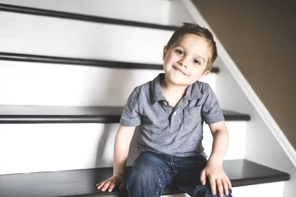 Niño pequeño sentado en las escaleras en casa durante el día . — Foto de Stock