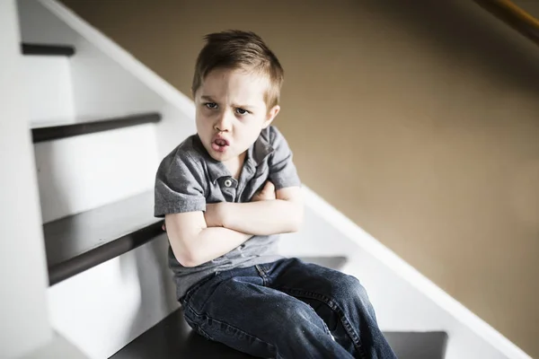 Один сумний маленький хлопчик сидить на сходах в будинку в день . — стокове фото