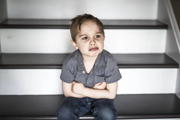 En ledsen liten pojke sitter på trappan i huset på dagtid. — Stockfoto