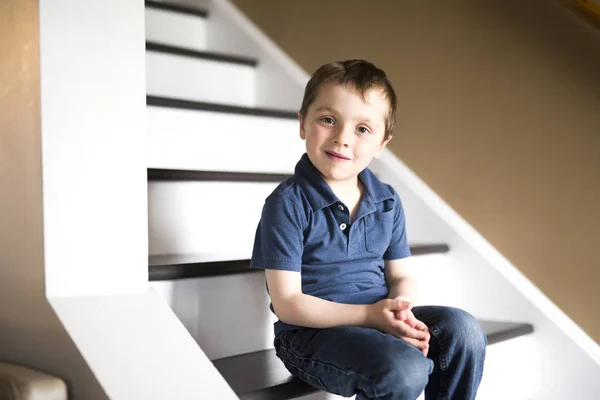 Niño pequeño sentado en las escaleras en casa durante el día . —  Fotos de Stock