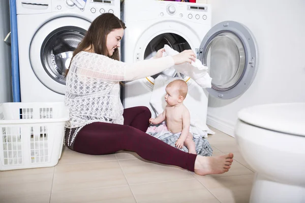 Anya a háziasszony, a baba végző mosoda fold ruhát a mosógép — Stock Fotó