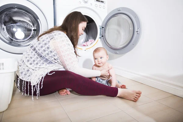 Mère une femme au foyer avec un bébé engagé dans la blanchisserie plier les vêtements dans la machine à laver — Photo