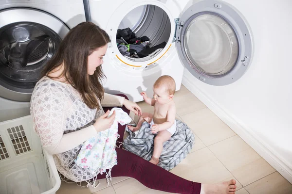 Mère une femme au foyer avec un bébé engagé dans la blanchisserie plier les vêtements dans la machine à laver — Photo