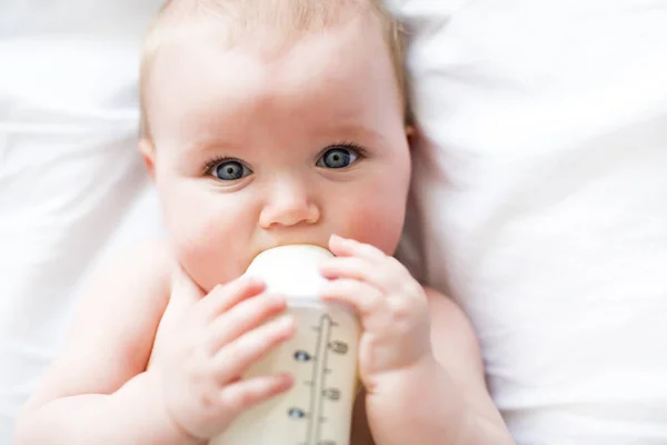 Jolie petite fille boit de l'eau du biberon couché sur le lit. Couche portée enfant dans la chambre d'enfant . — Photo