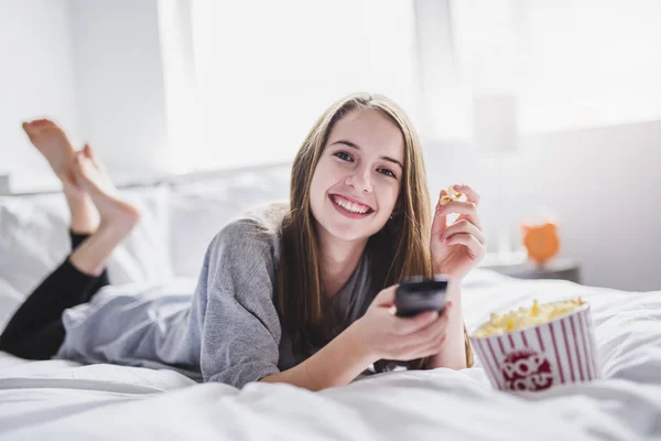 Jovem adolescente assistindo filmes na cama com pipocas — Fotografia de Stock