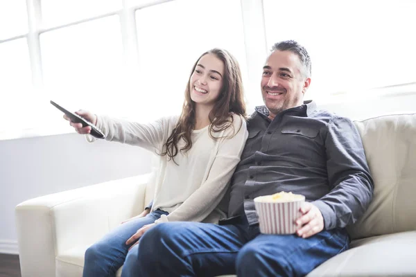 Porträtt av en ung man och dotter titta på Tv medan man äter popcorn i soffan — Stockfoto