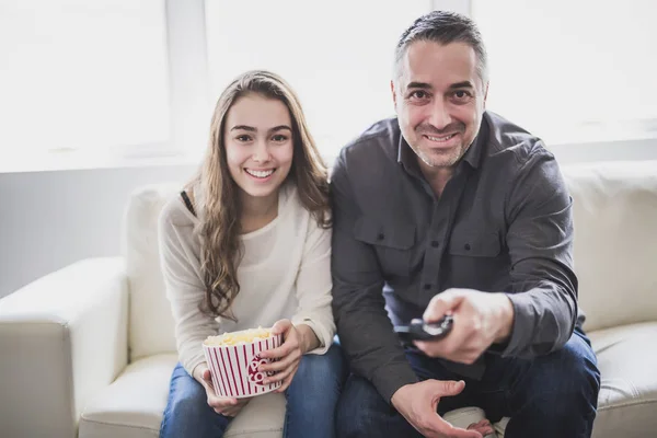 Retrato de um jovem e filha assistindo TV enquanto come pipocas no sofá — Fotografia de Stock