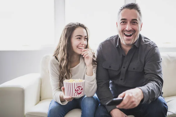 Porträtt av en ung man och dotter titta på Tv medan man äter popcorn i soffan — Stockfoto