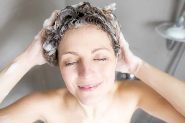 Duşta şampuanla saç yıkayan bir kadın. — Stok fotoğraf