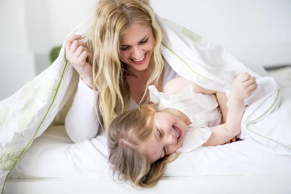 Menina bonito e sua mãe deitada em uma cama — Fotografia de Stock