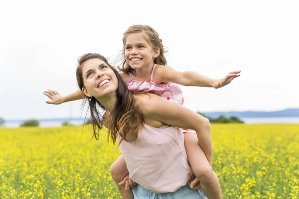 Happy family mother and child daughter embrace on yellow flowers on nature in summer — Stock Photo, Image