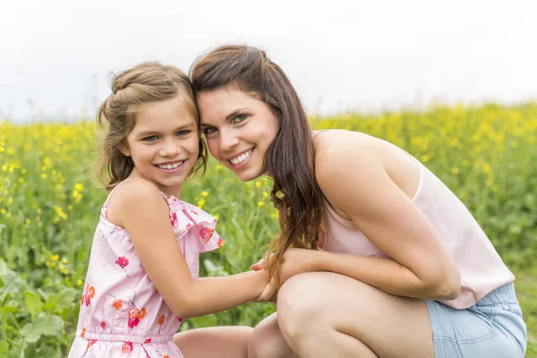 Glückliche Familie Mutter und Kind Tochter Umarmung auf gelben Blumen in der Natur im Sommer — Stockfoto