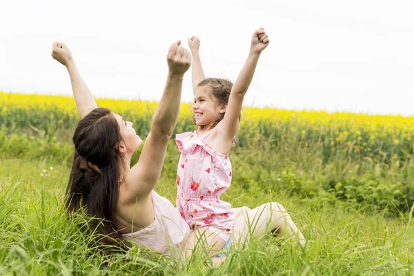 Happy family mother and child daughter embrace on yellow flowers on nature in summer — Stock Photo, Image