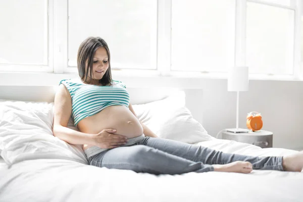 Beautiful pregnant woman posing while lying on a bed at home — Stock Photo, Image