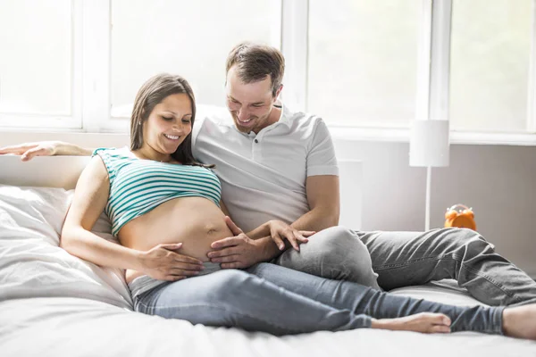 Unga föräldrar i sängen väntar en liten baby, romantiska stunder för gravida par — Stockfoto