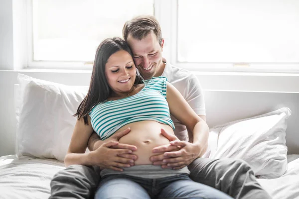 Unga föräldrar i sängen väntar en liten baby, romantiska stunder för gravida par — Stockfoto