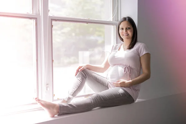 Junge schöne schwangere Frau sitzt zu Hause auf Fensterbank — Stockfoto