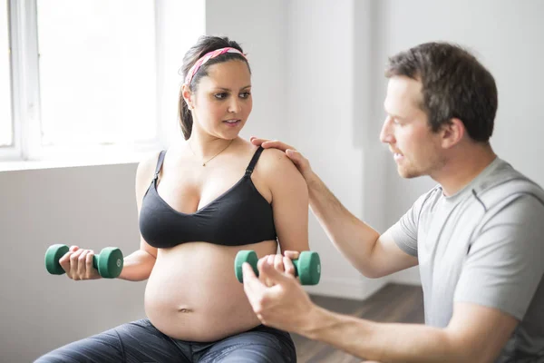 Mulher grávida trabalhando com halteres com personal trainer no ginásio — Fotografia de Stock