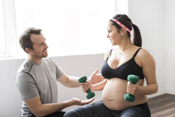 Беременная женщина работает с гантелями с личным тренером в тренажерном зале — стоковое фото