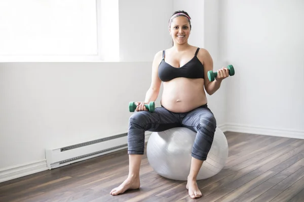 Беременная женщина тренируется с гантелями, чтобы оставаться активной — стоковое фото