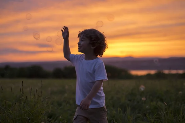 Băiat lovit balon pe o pajiște apus de soare — Fotografie, imagine de stoc