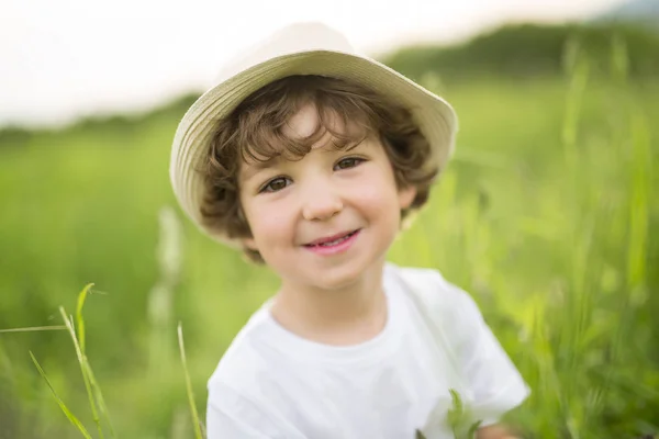 Porträtt av bedårande kid pojke med hatt står på en sommaräng — Stockfoto