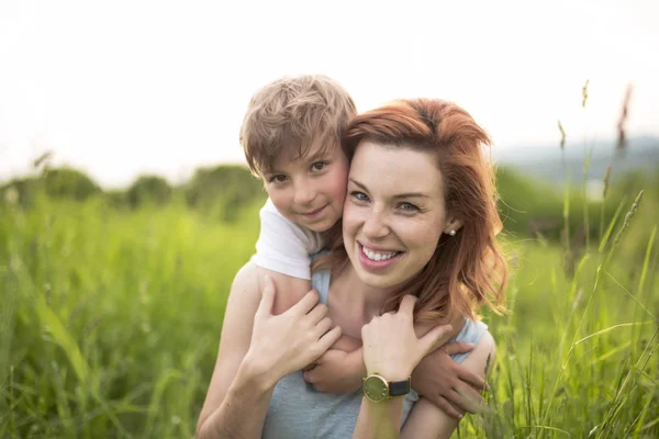 Rapaz bonito com sua mãe em um prado de verão — Fotografia de Stock
