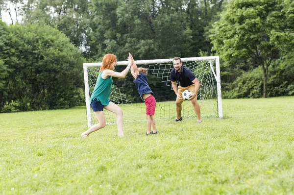 Família alegre jogando futebol em um parque — Fotografia de Stock