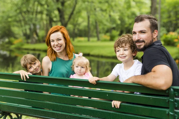 Счастливая семья сидит на скамейке в парке — стоковое фото