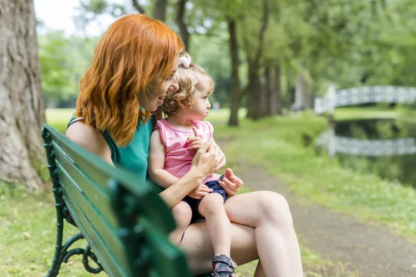 Mother and her little daughter sitting on a park bench — Stock Photo, Image