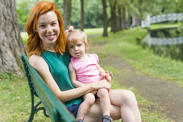 Mother and her little daughter sitting on a park bench — Stock Photo, Image