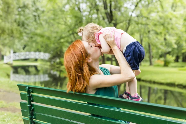 Mother and her little daughter sitting on a park bench — Stock Photo, Image