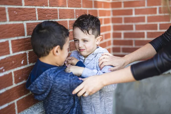 Professor interrompendo dois meninos lutando no parque infantil — Fotografia de Stock